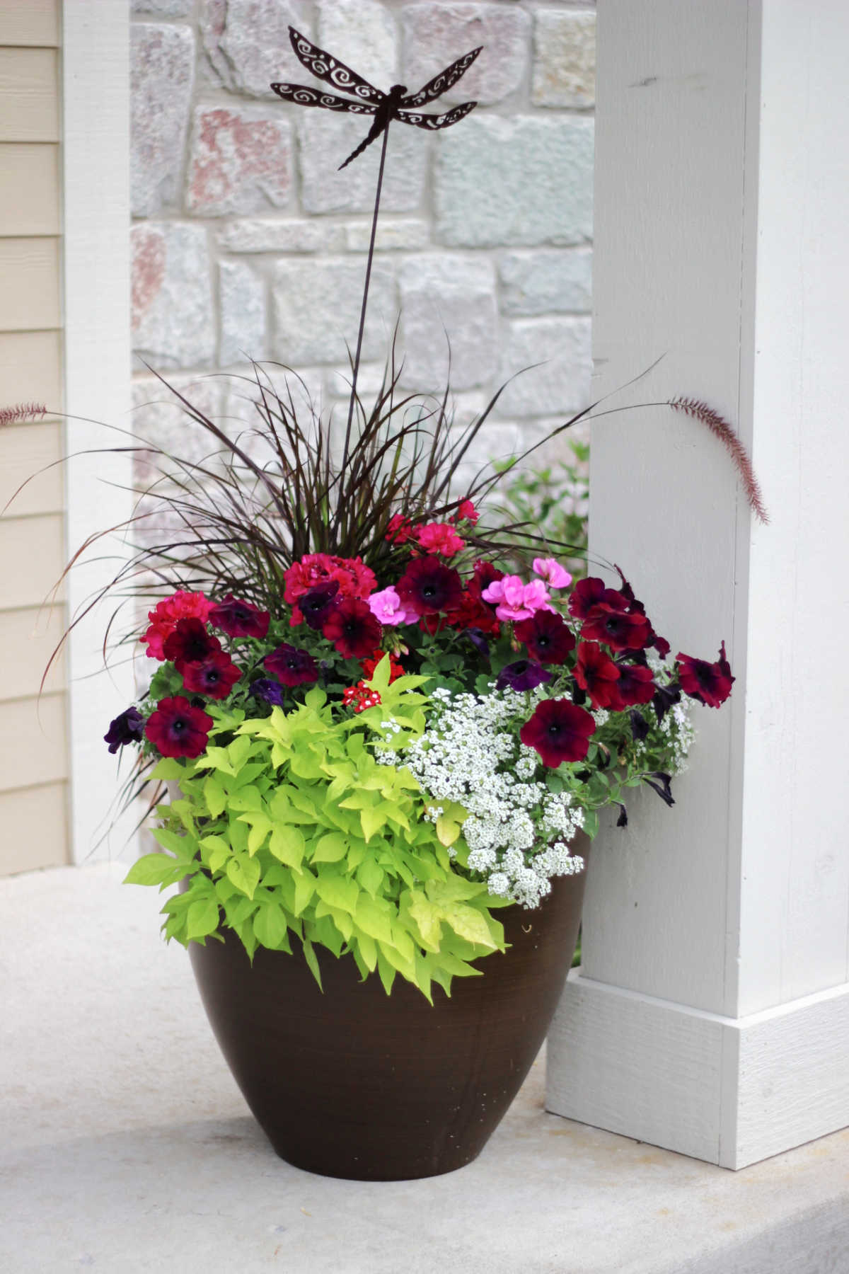 colorful flowers in a planter that gains extra height with a garden art stake of a dragonfly.